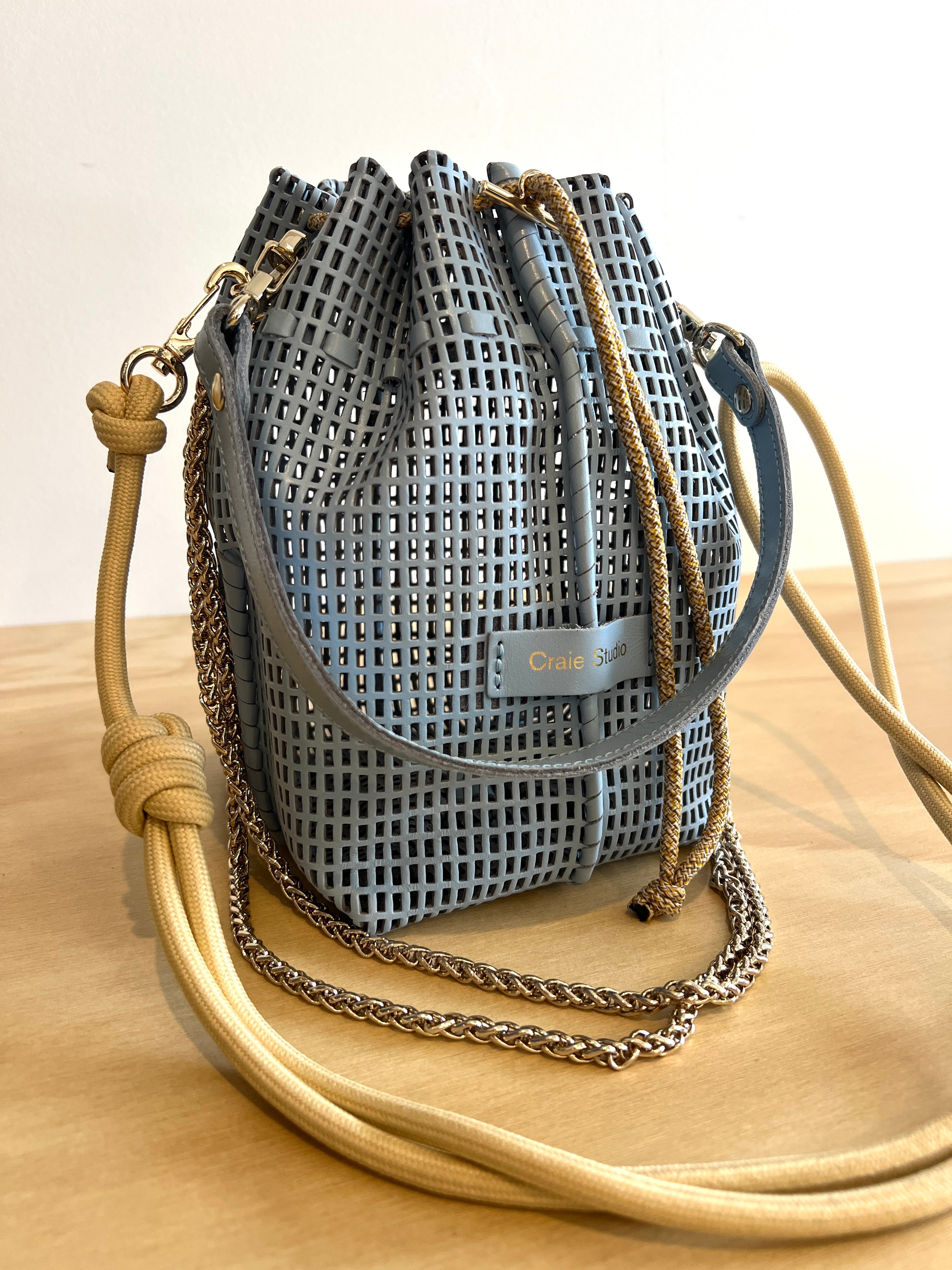 Blue woven drawstring bag with beige shoulder strap on a wooden surface