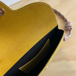 Close-up of a yellow leather pouch with a black interior on a beige surface.