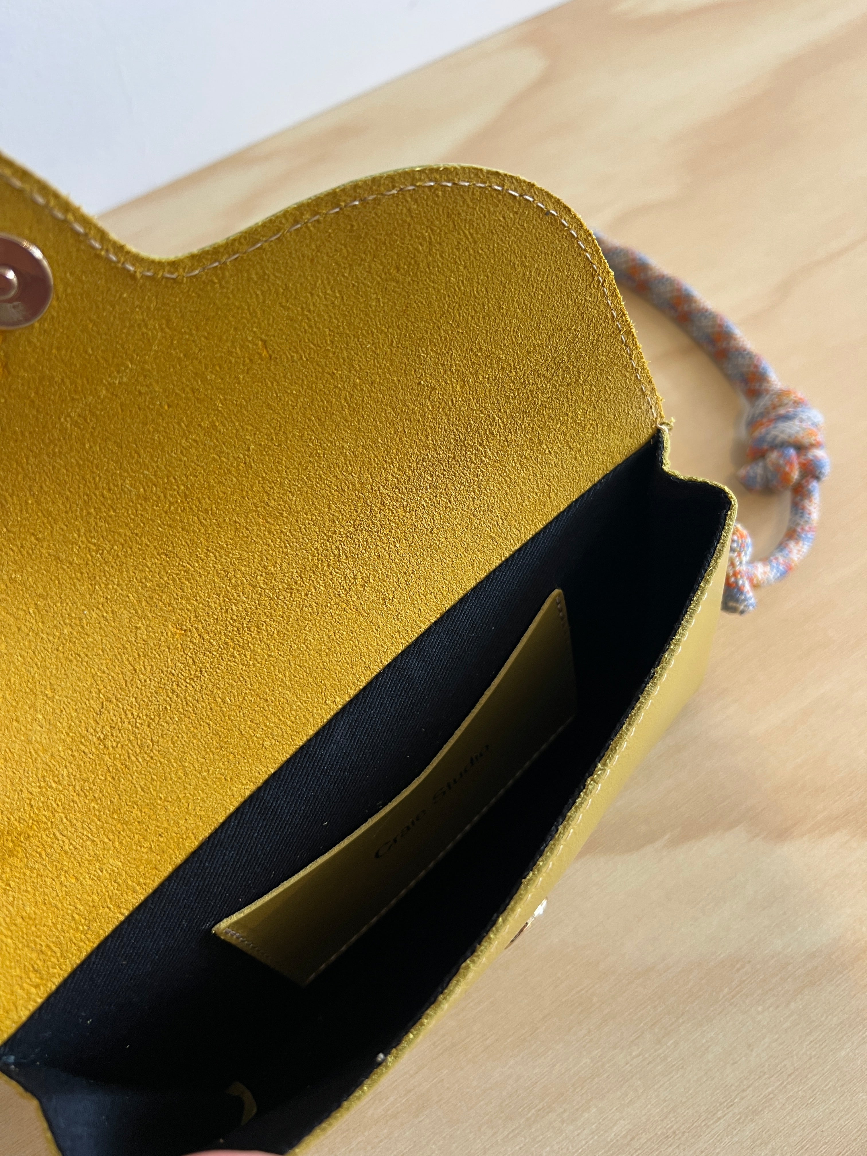 Close-up of a yellow leather pouch with a black interior on a beige surface.