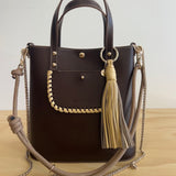 Brown handbag with tassels and a chain strap on a wooden surface
