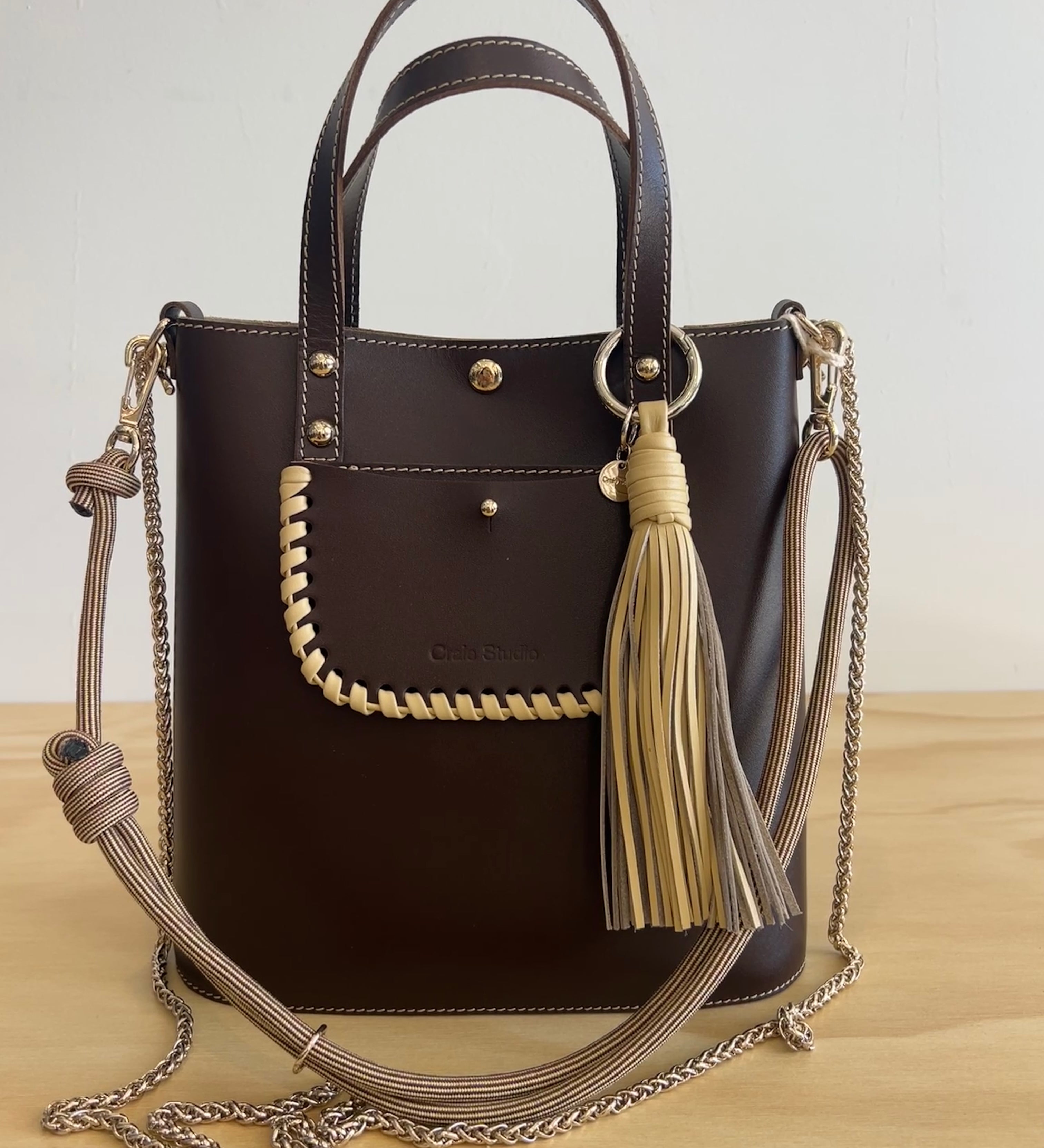 Brown handbag with tassels and a chain strap on a wooden surface