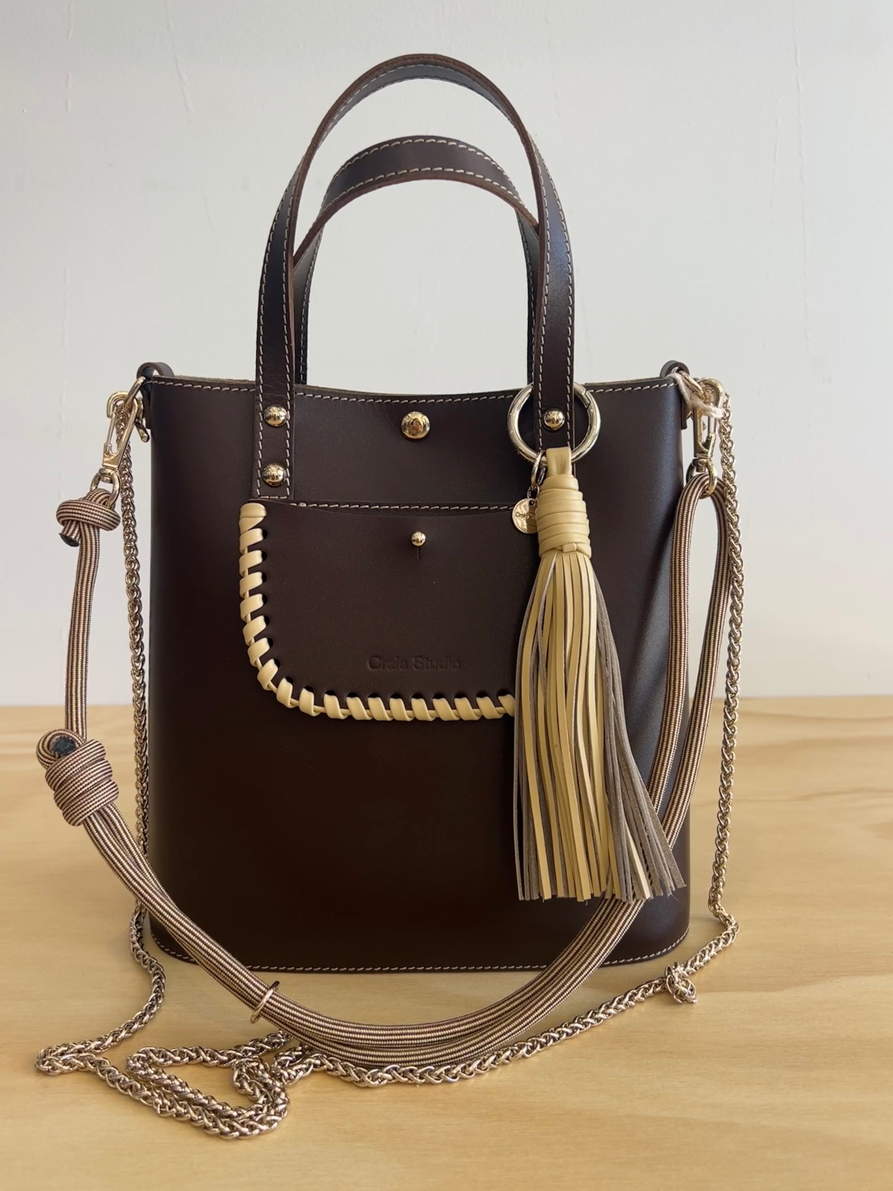 Brown handbag with tassels and a chain strap on a wooden surface