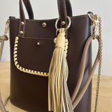 Brown handbag with gold chain strap and tassel on a light background