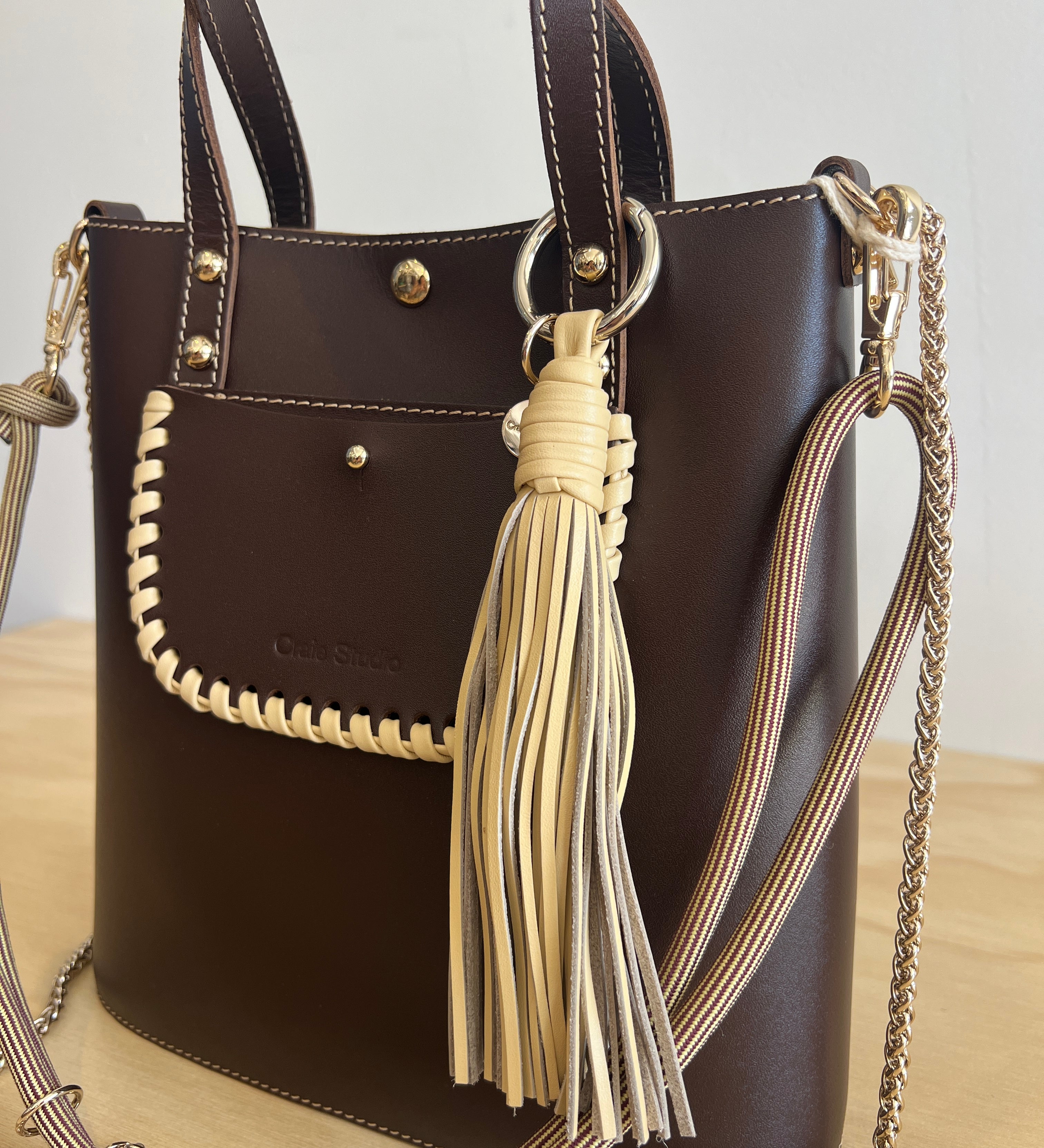 Brown handbag with gold chain strap and tassel on a light background