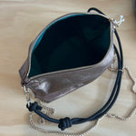 Silver handbag with a black strap on a wooden surface