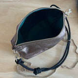 Silver handbag with a black strap on a wooden surface