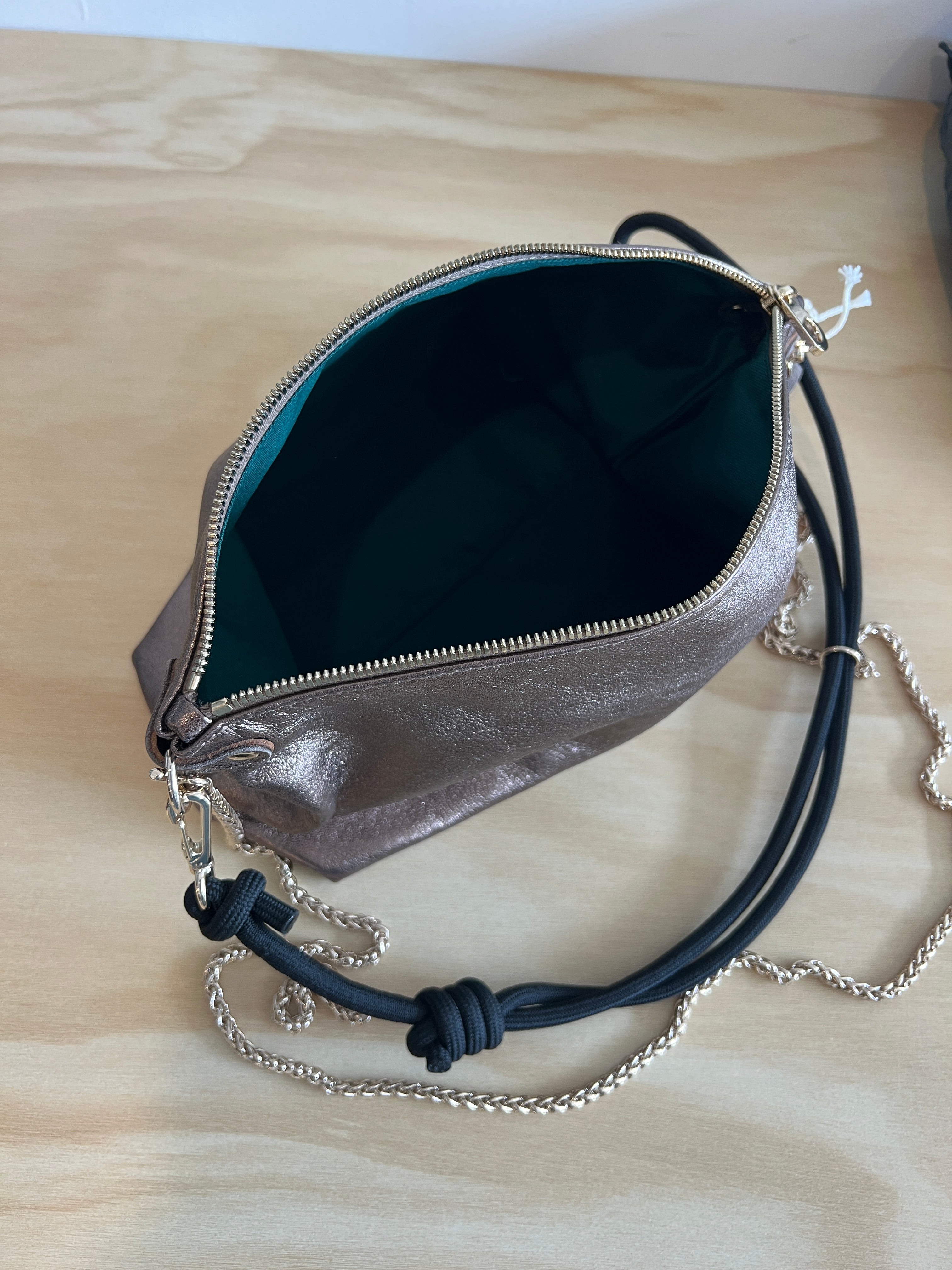Silver handbag with a black strap on a wooden surface