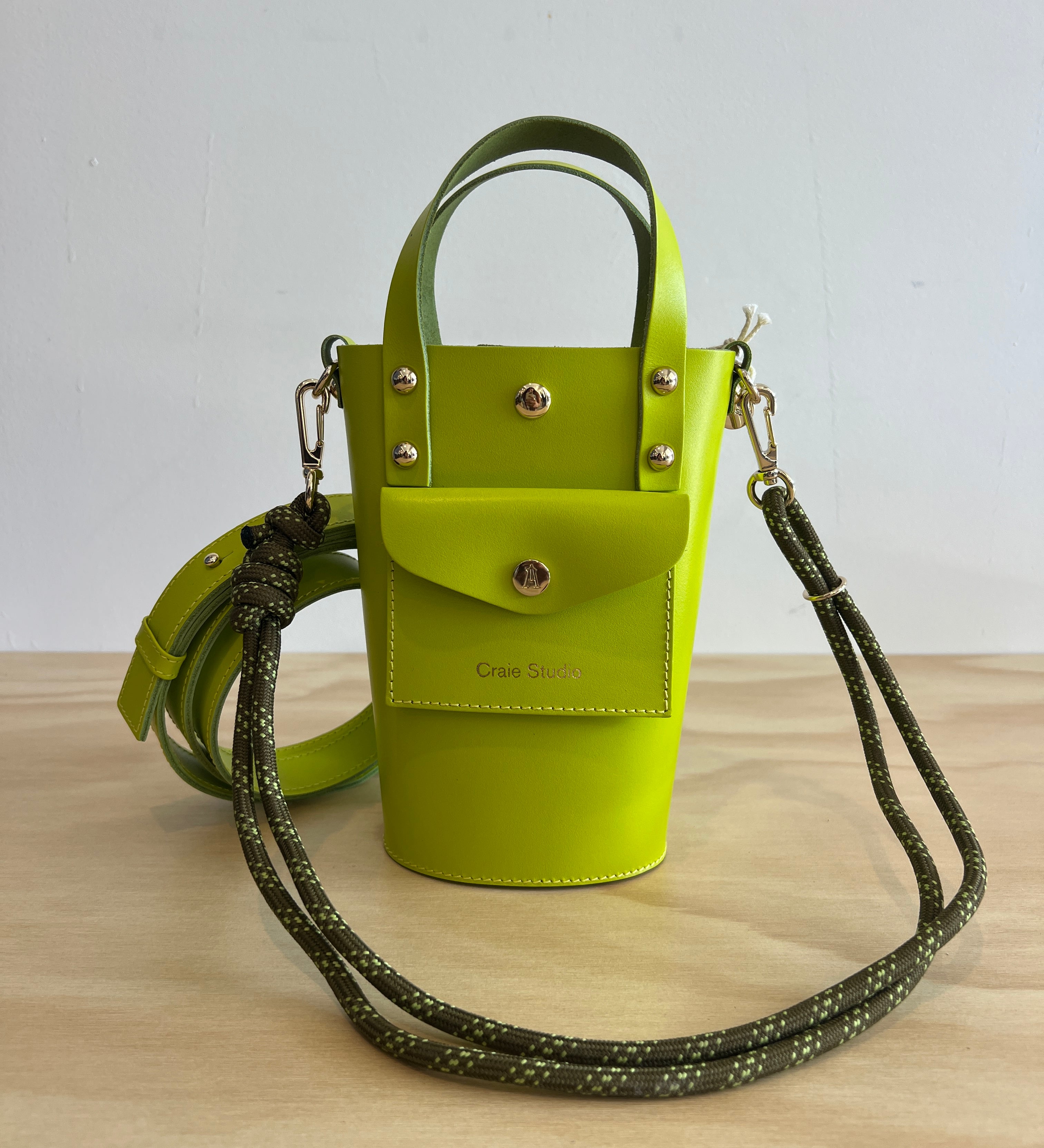Green handbag with a strap on a light wooden surface