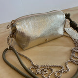 Gold metallic clutch bag with a chain strap on a light wooden surface.