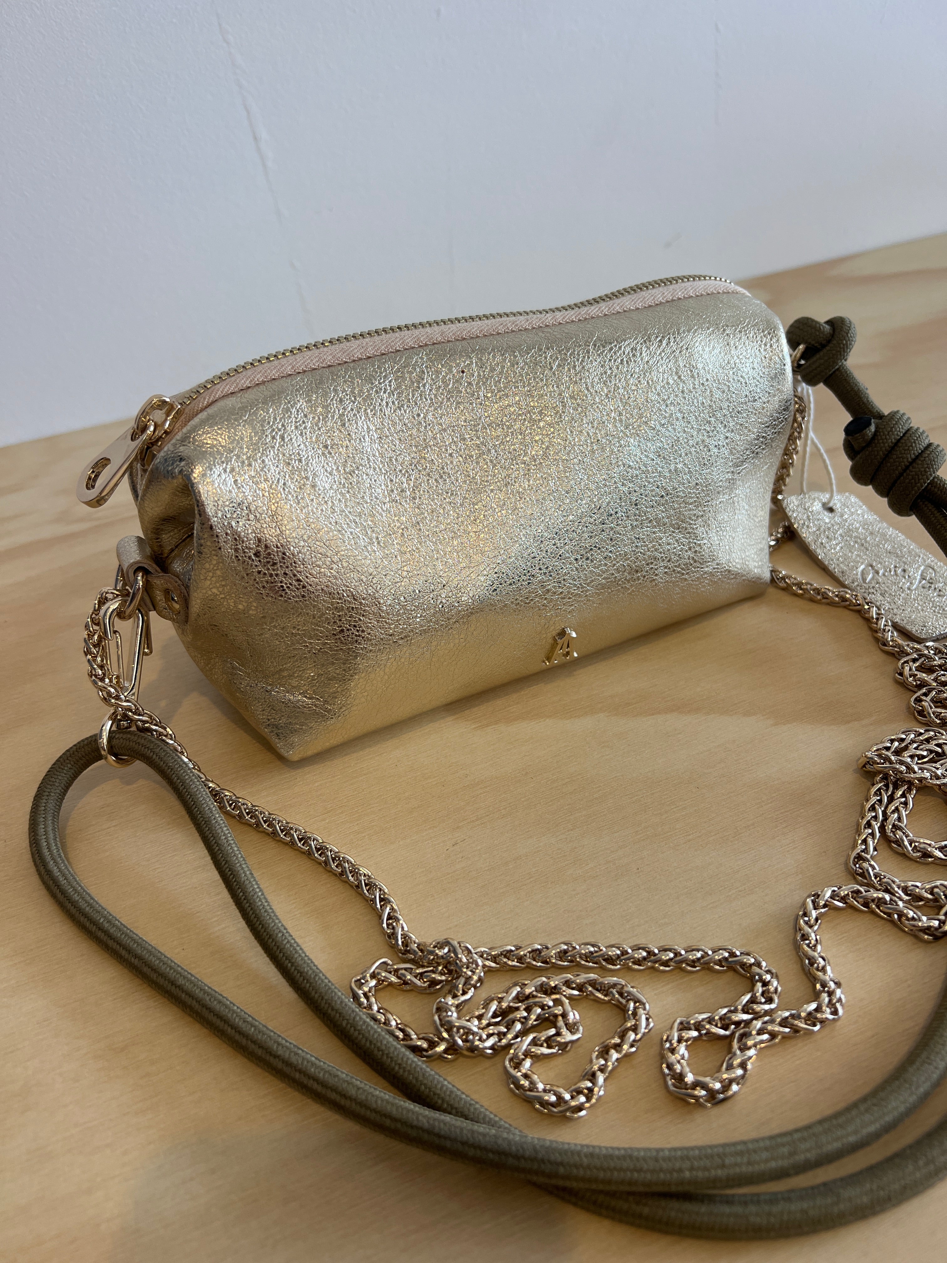 Gold metallic clutch bag with a chain strap on a light wooden surface.