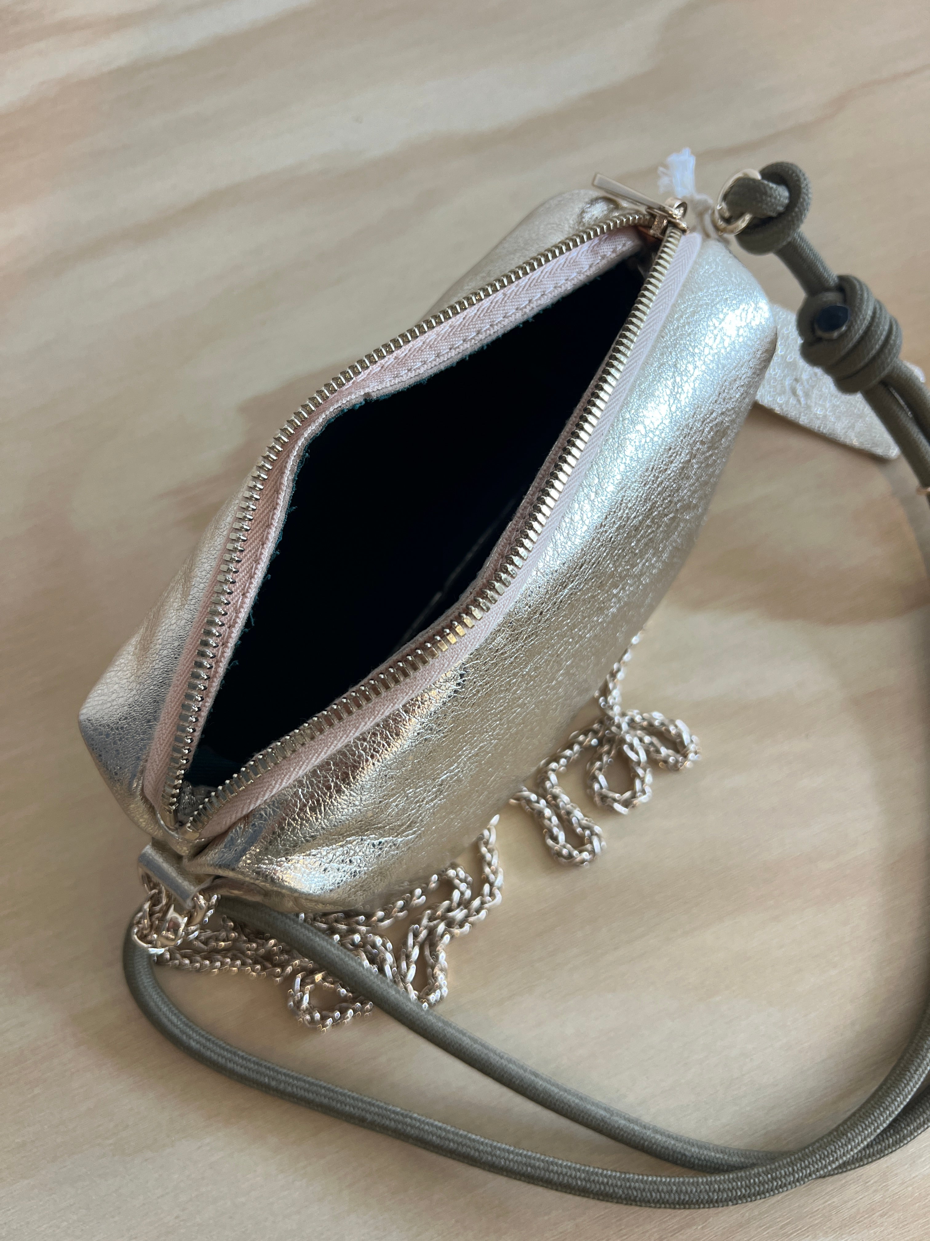 Gold metallic clutch bag with chain detail on a beige surface