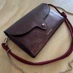 Brown leather handbag with a red strap on a light wooden surface