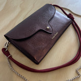 Brown leather handbag with a red strap on a light wooden surface