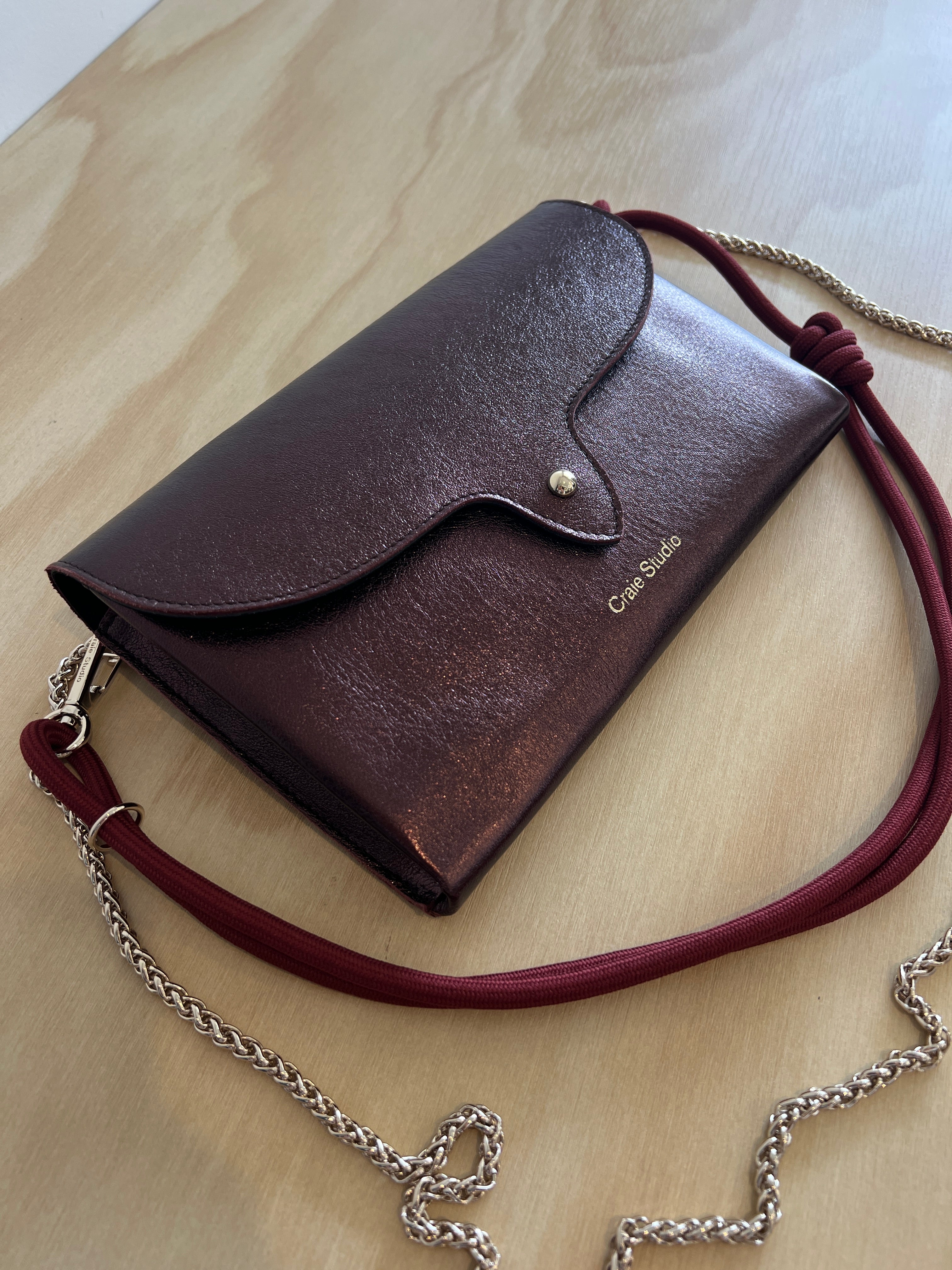 Brown leather handbag with a red strap on a light wooden surface