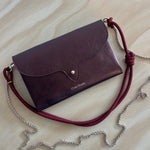 Leather handbag with a red strap and silver chain on a beige surface