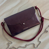 Leather handbag with a red strap and silver chain on a beige surface