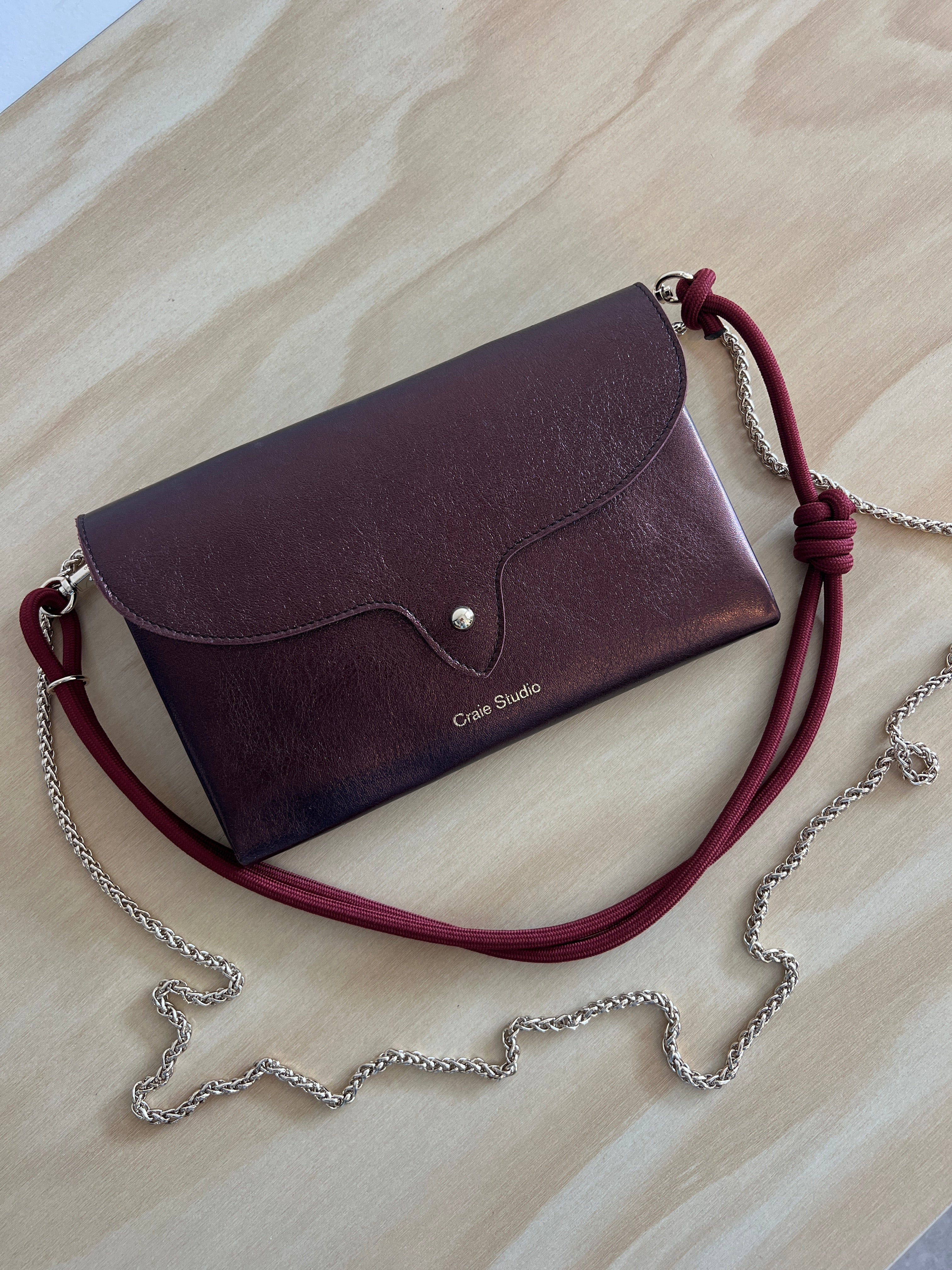 Leather handbag with a red strap and silver chain on a beige surface