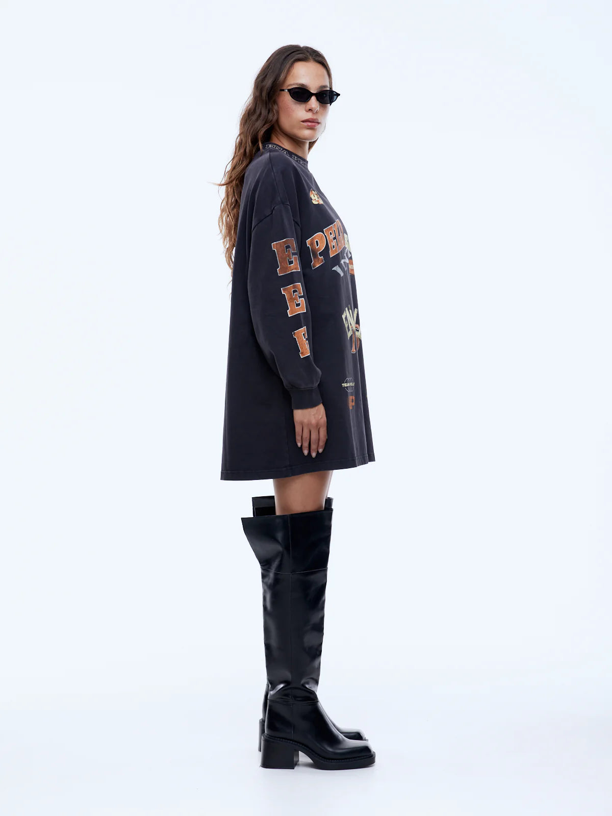 Woman wearing a black oversized sweatshirt with text and black knee-high boots on a white background