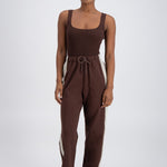 A model wearing chocolate brown trackpants with a relaxed fit, elastic waistband with drawstring, and pockets.