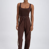 A model wearing chocolate brown trackpants with a relaxed fit, elastic waistband with drawstring, and pockets.