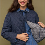 Woman wearing a navy quilted jacket over a denim dress, holding a checkered lining.