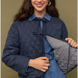 Woman wearing a navy quilted jacket over a denim dress, holding a checkered lining.