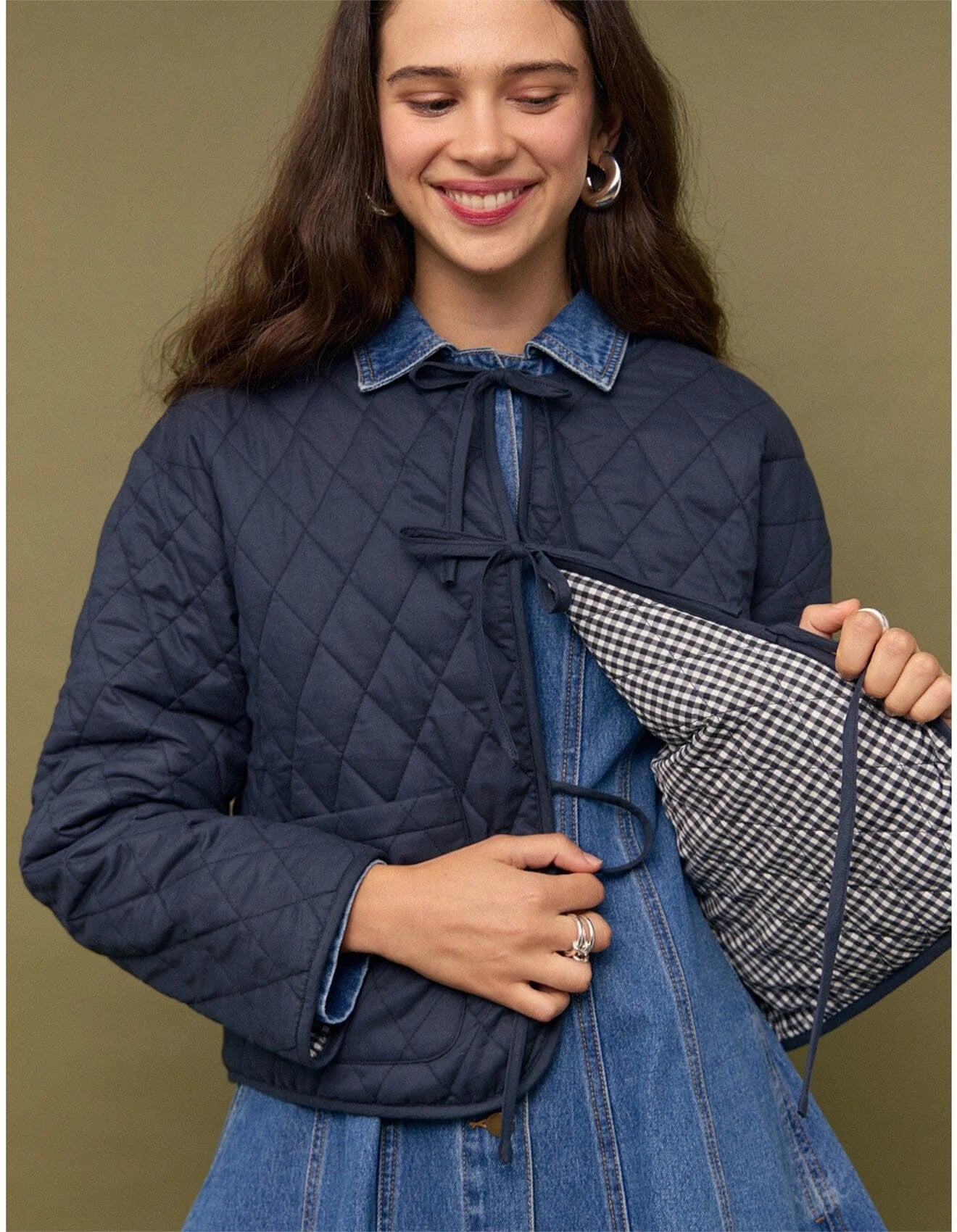 Woman wearing a navy quilted jacket over a denim dress, holding a checkered lining.