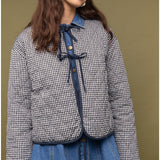 Woman wearing a checkered jacket and blue jeans against a brown background