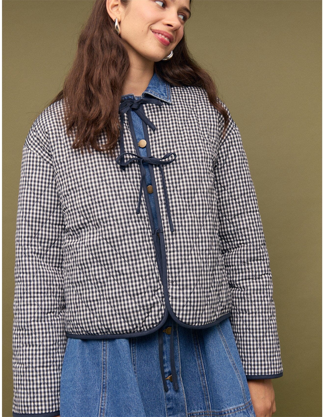 Woman wearing a checkered jacket and blue jeans against a brown background