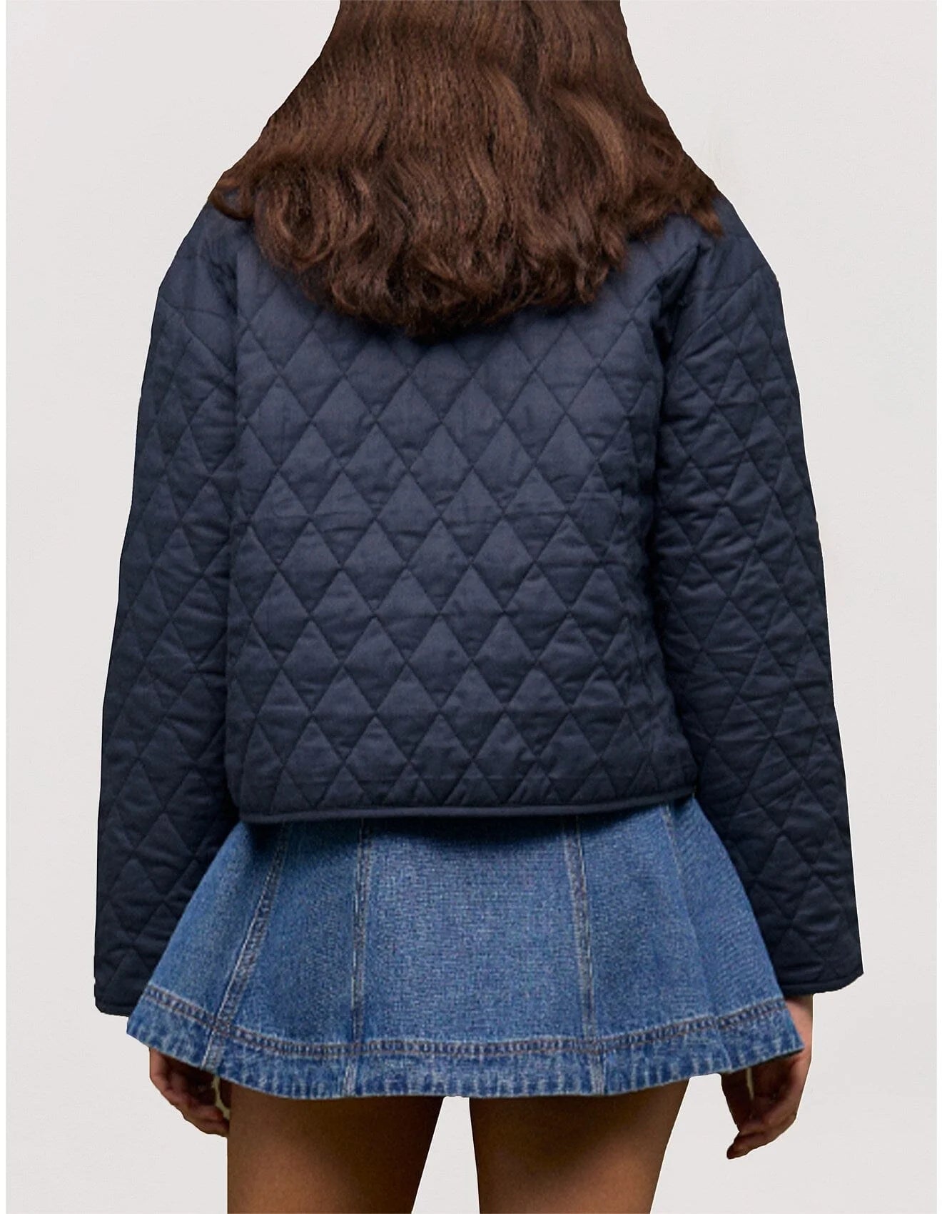 Person wearing a navy quilted jacket and denim skirt on a light gray background