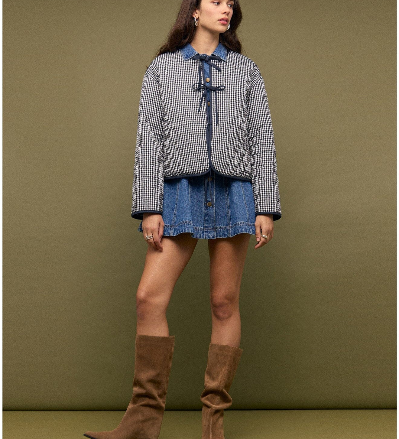 Woman wearing a checkered jacket, denim skirt, and brown knee-high boots against a green background