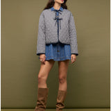 Woman wearing a checkered jacket, denim skirt, and brown knee-high boots against a green background