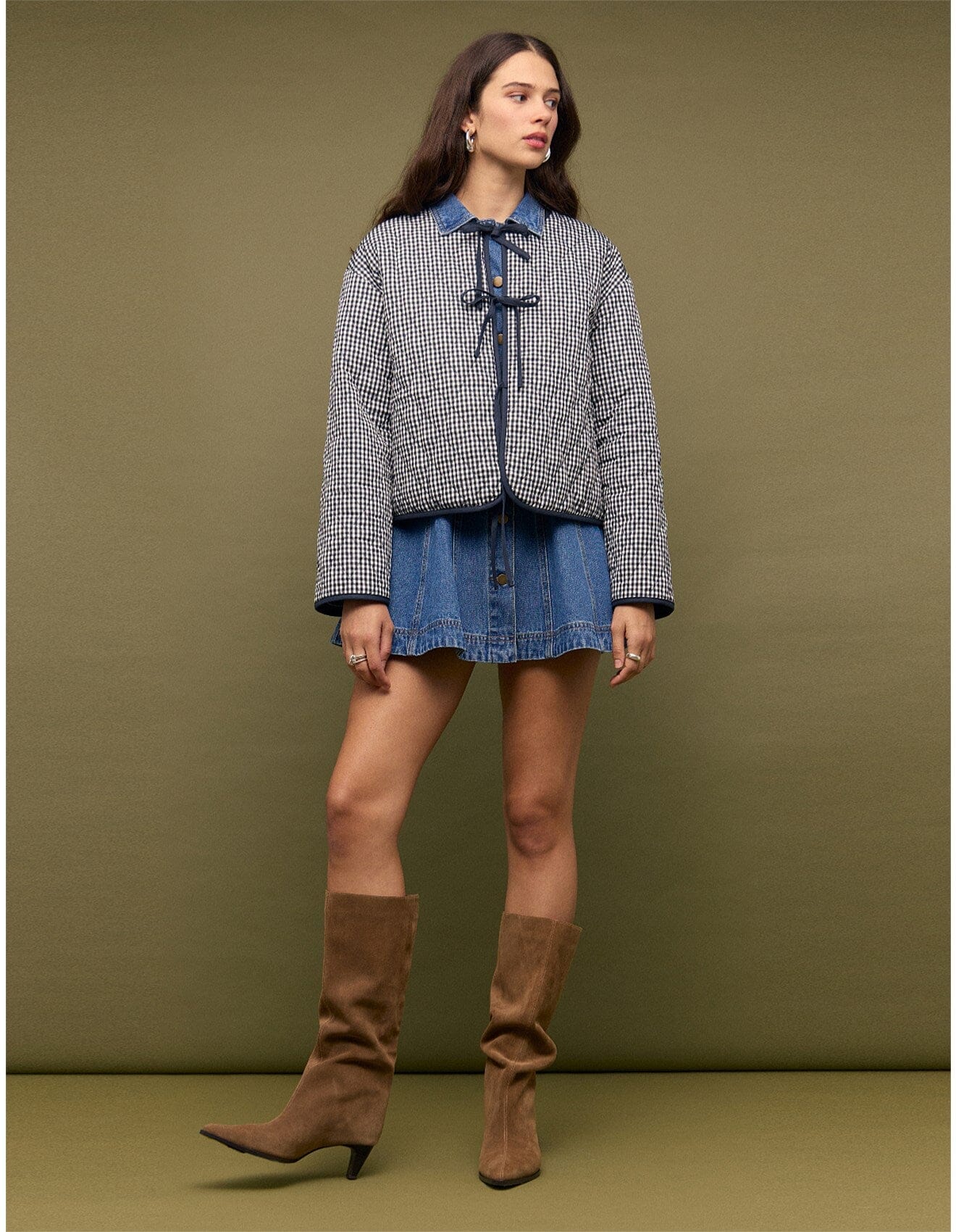 Woman wearing a checkered jacket, denim skirt, and brown knee-high boots against a green background