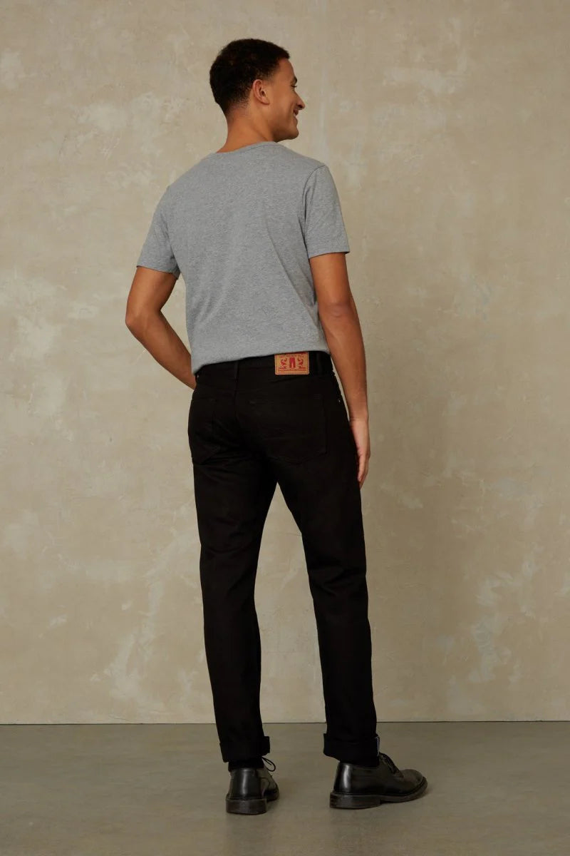 Man wearing a gray t-shirt and black pants against a beige wall