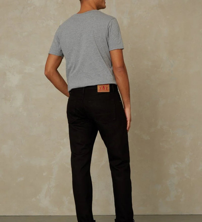 Man wearing a gray t-shirt and black pants against a beige wall