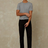 Man wearing a gray t-shirt and black pants standing against a beige wall.