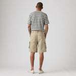 A man viewed from behind wearing a navy and white striped t-shirt, beige cargo shorts, and white sneakers, standing against a light gray studio background.