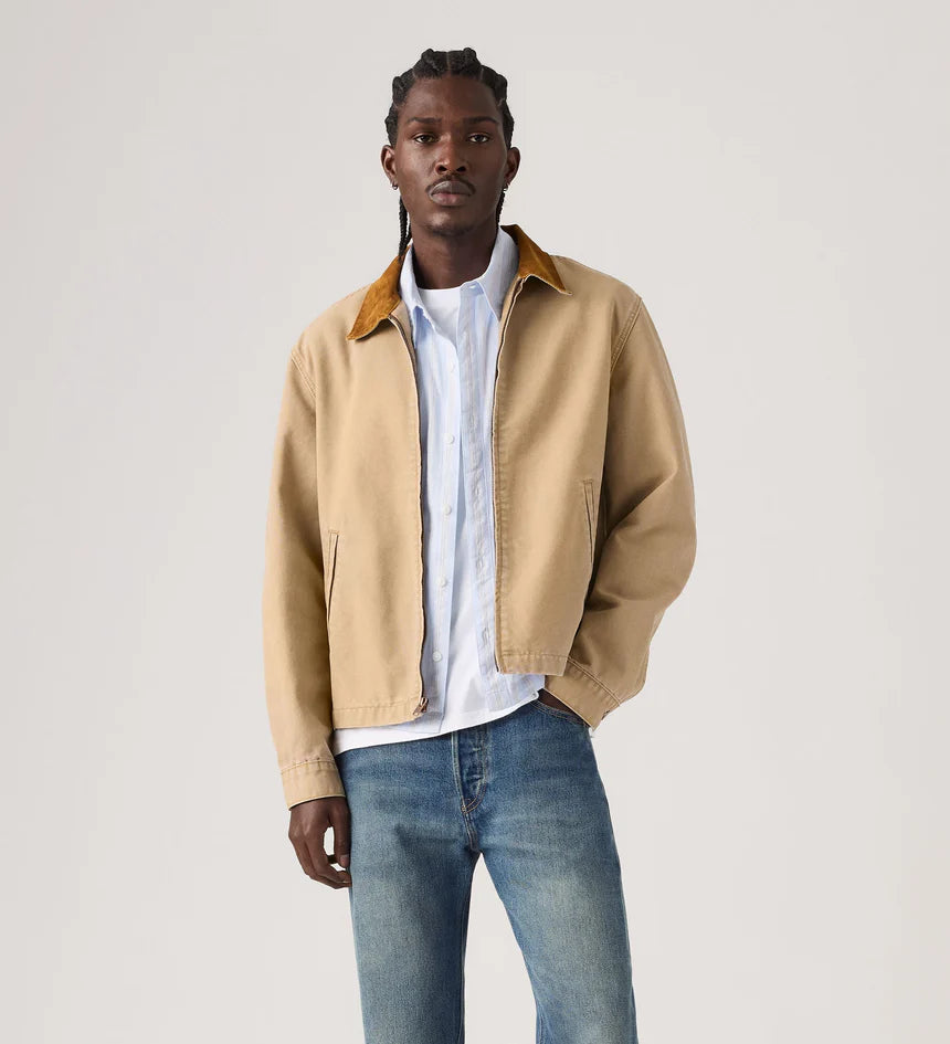 Man wearing a beige jacket, white shirt, and blue jeans on a light gray background