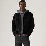 Man wearing a black denim jacket over a gray hoodie on a plain background