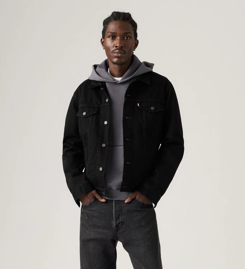 Man wearing a black denim jacket over a gray hoodie on a plain background