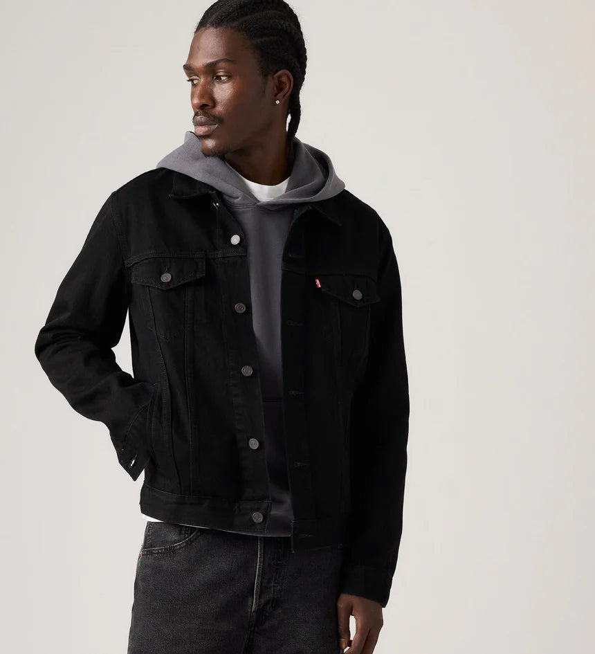 Man wearing a black denim jacket over a gray hoodie on a plain background