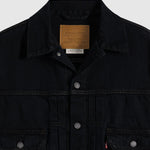 Close-up of a black Levi's denim jacket showing the collar, inner brand patch, snap-button front, and chest pockets on a light gray background.