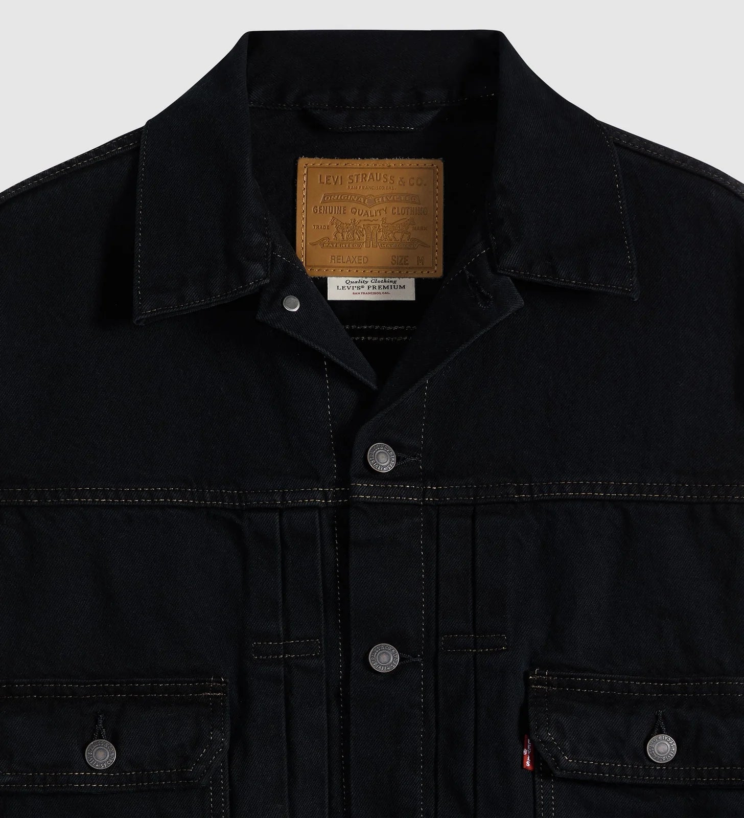Close-up of a black Levi's denim jacket showing the collar, inner brand patch, snap-button front, and chest pockets on a light gray background.