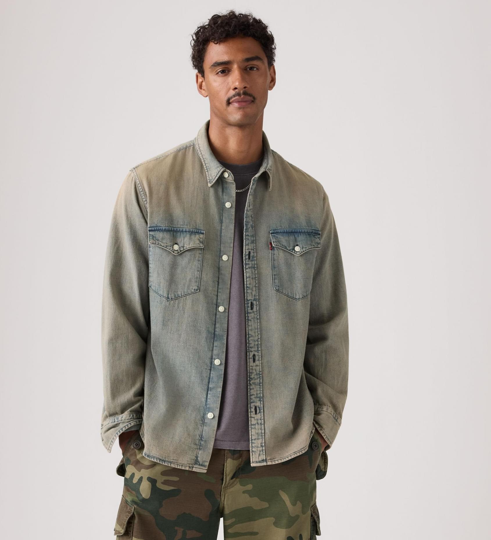 Man wearing a denim jacket and camouflage pants on a plain background