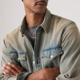 Man wearing a light denim jacket over a gray shirt against a neutral background