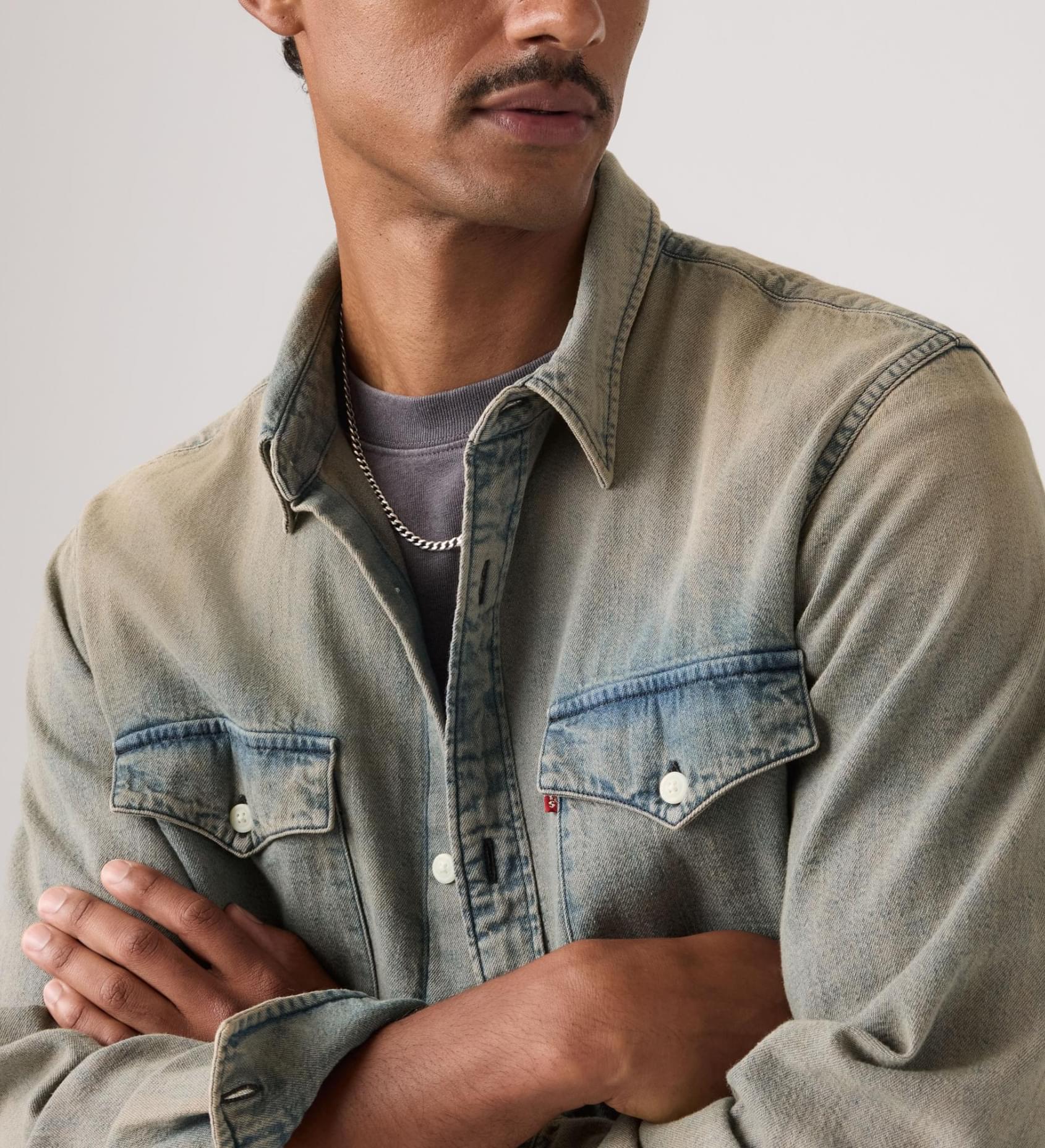 Man wearing a light denim jacket over a gray shirt against a neutral background