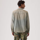 Man wearing a green denim shirt and camouflage pants on a white background