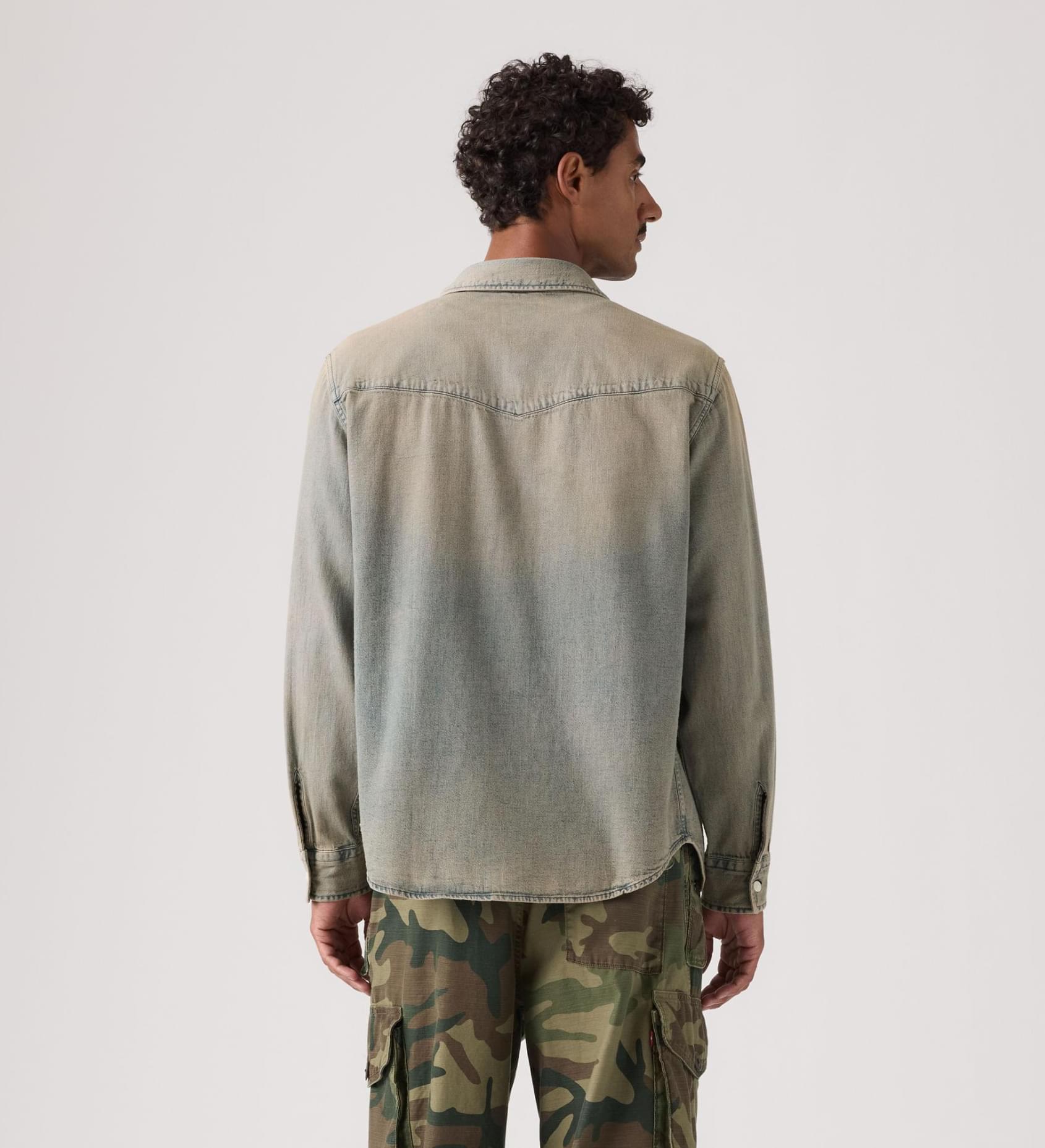 Man wearing a green denim shirt and camouflage pants on a white background