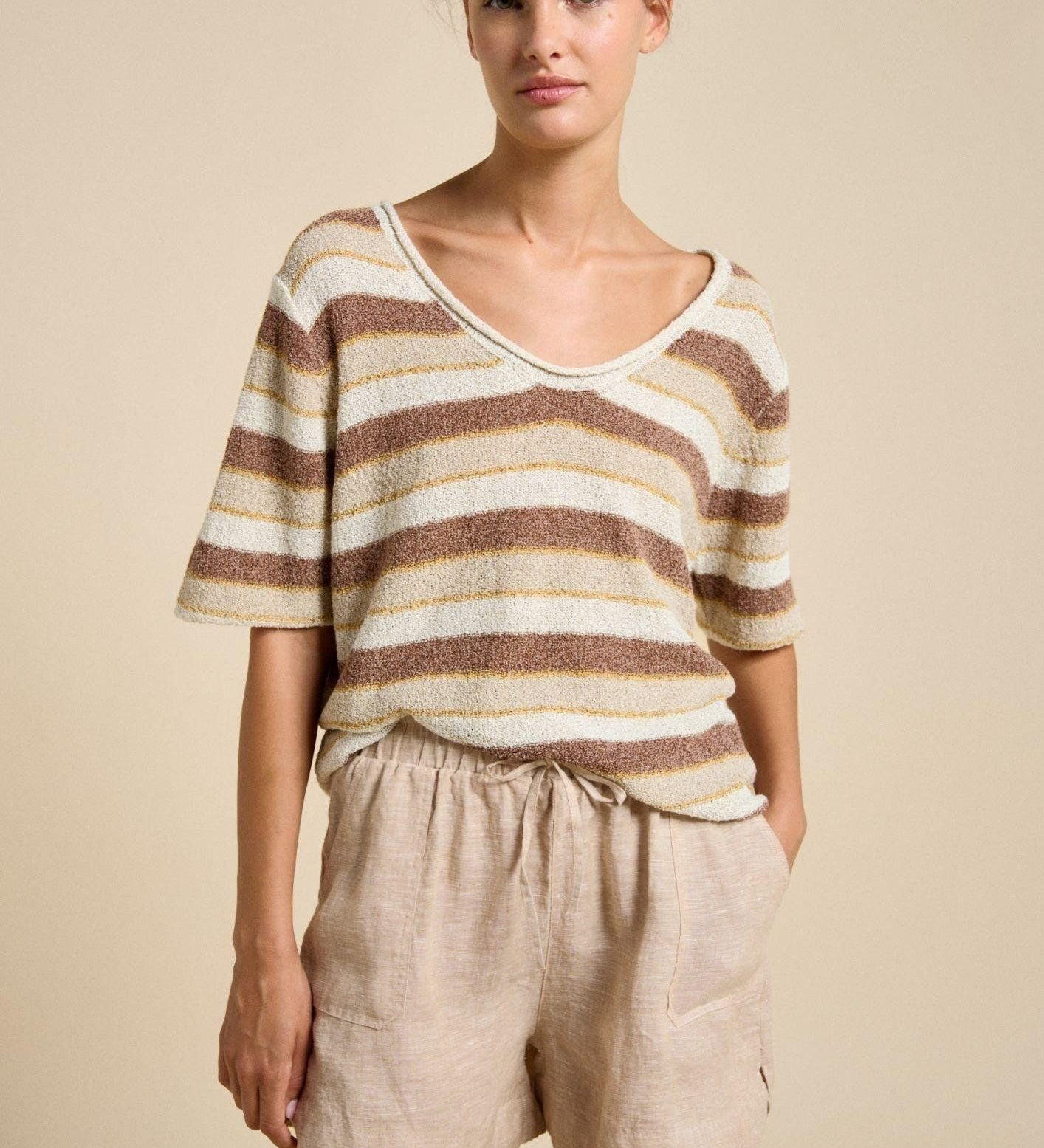 Woman wearing a striped shirt and beige shorts against a beige background