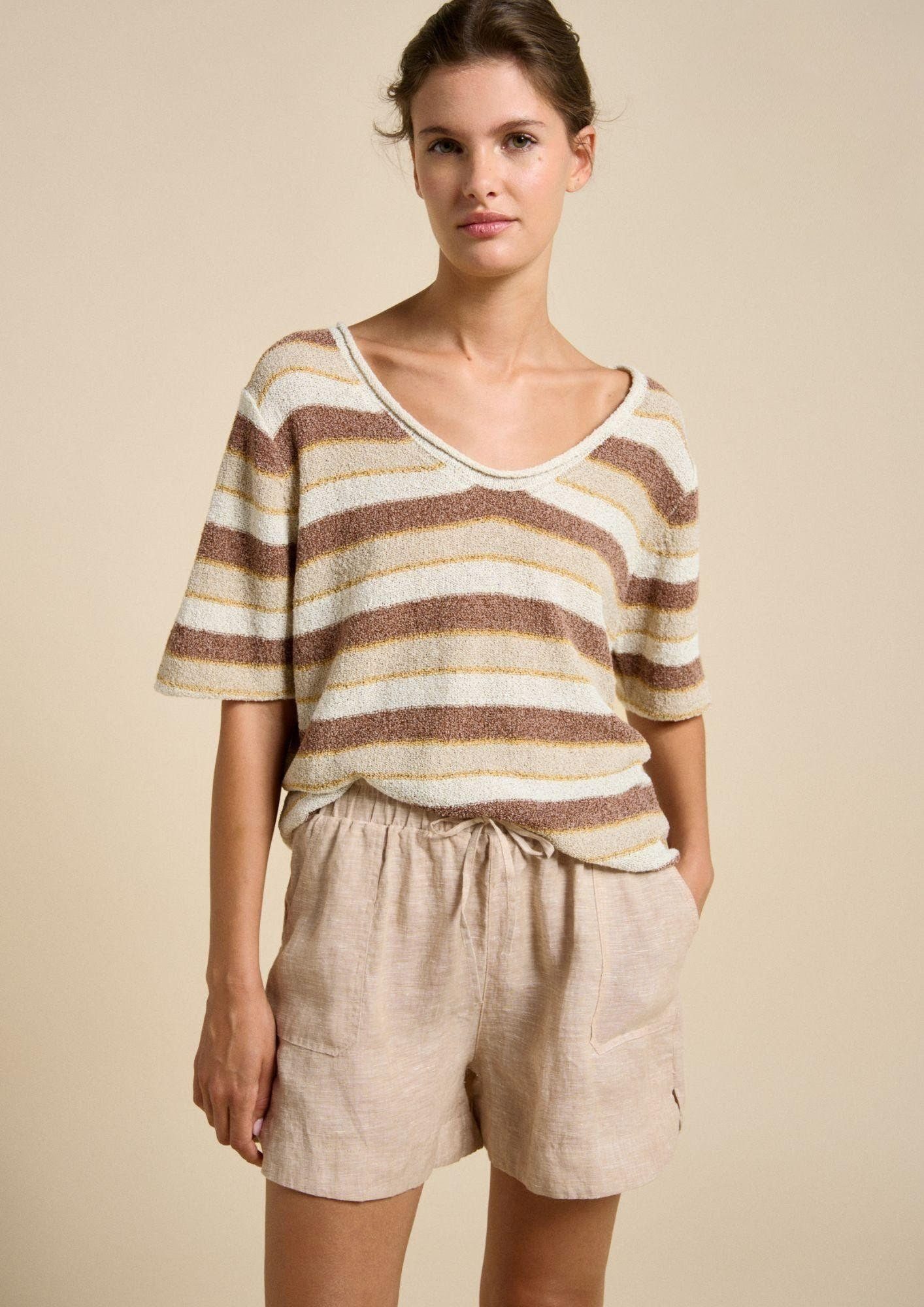 Woman wearing a striped shirt and beige shorts against a beige background